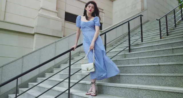 Han So-hee standing on stairs in a blue dress and sandals.
