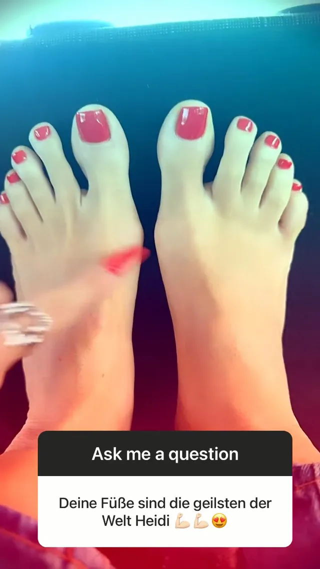 Heidi Klum raising her bare feet with red-painted toenails while travelling.