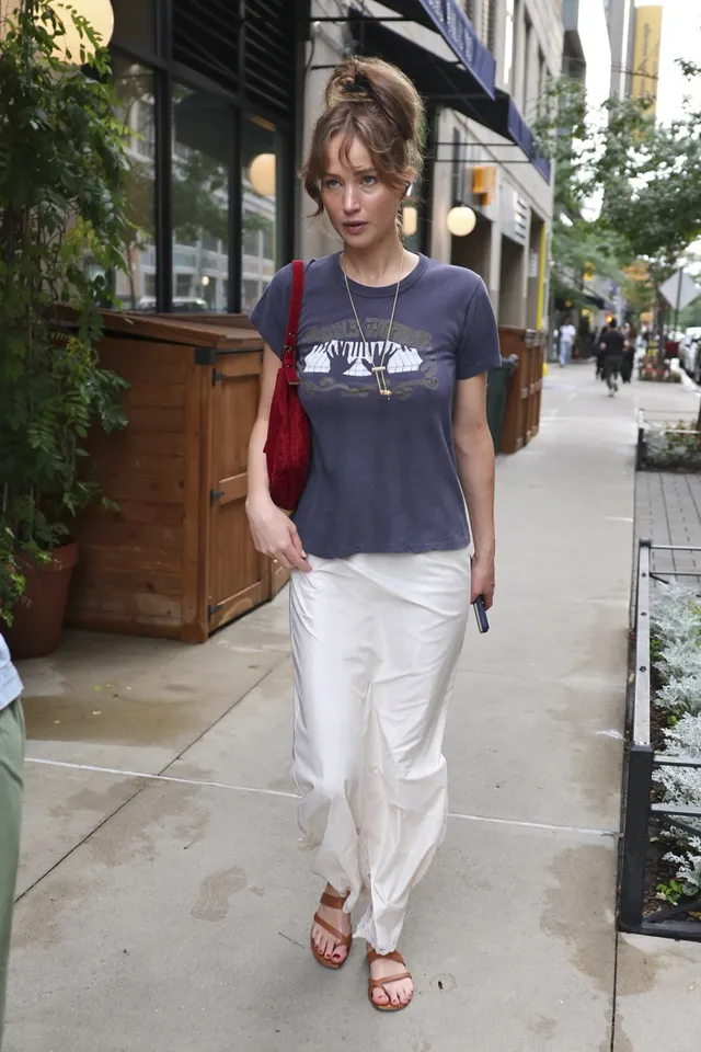 Jennifer Lawrence walking outside in a T-shirt and flat sandals.