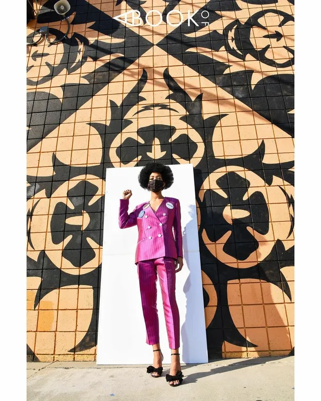 Samantha Logan posing before a mural in a pink trouser suit and black heels.