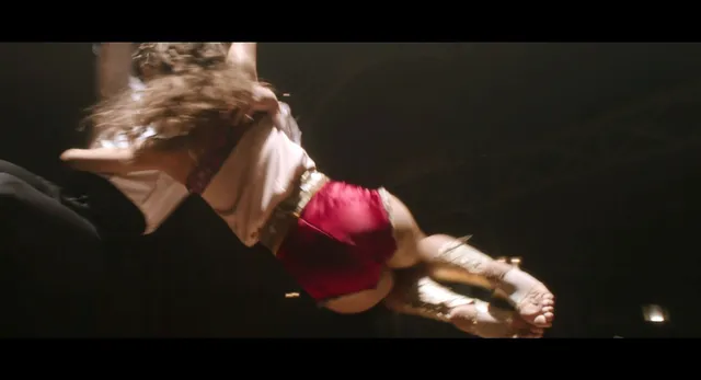 Zendaya lying barefoot on a floor in a dark film scene.