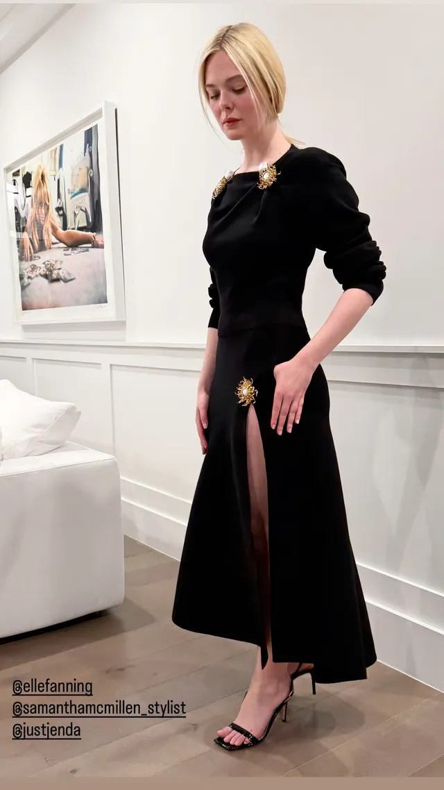 Elle Fanning wearing a long black dress and heeled sandals indoors.