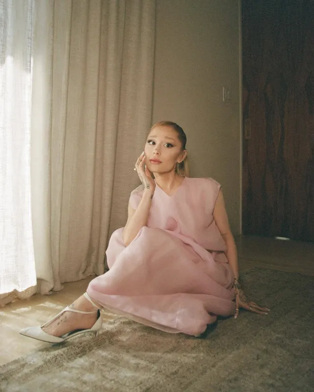 Ariana Grande sitting on a floor in a pink dress.
