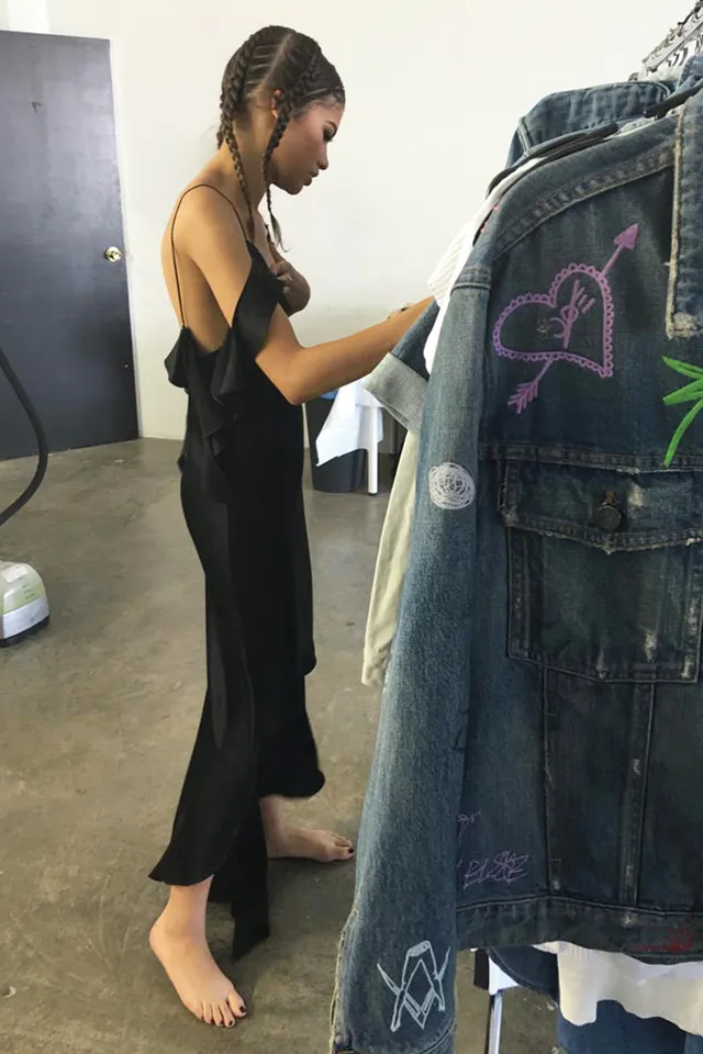 Zendaya: standing barefoot beside hanging clothes.