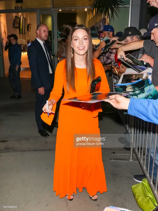 Victoria Pedretti signing items for fans in a long orange dress.