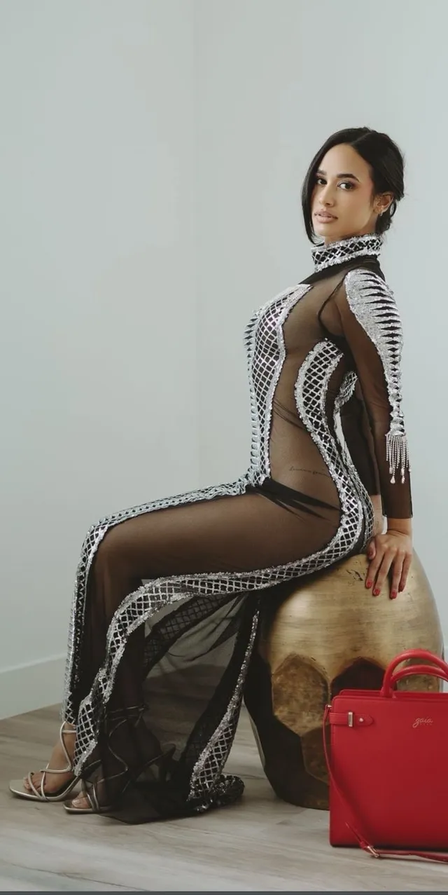Emily Tosta sitting in a patterned gown and heels.