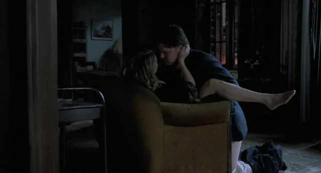 Léa Seydoux resting a leg beside a seated man in a screen scene.