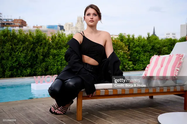 Nicole Wallace crouching beside a pool lounger in a black outfit and heels.