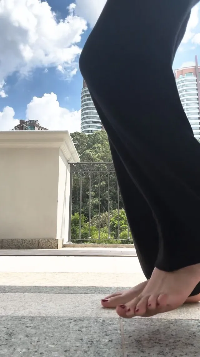 Olivia Rodrigo: standing barefoot on outdoor paving in black trousers.