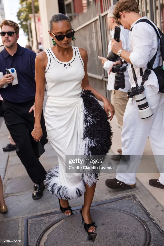 Sophie Wilde standing outdoors in a white dress and black heeled sandals.