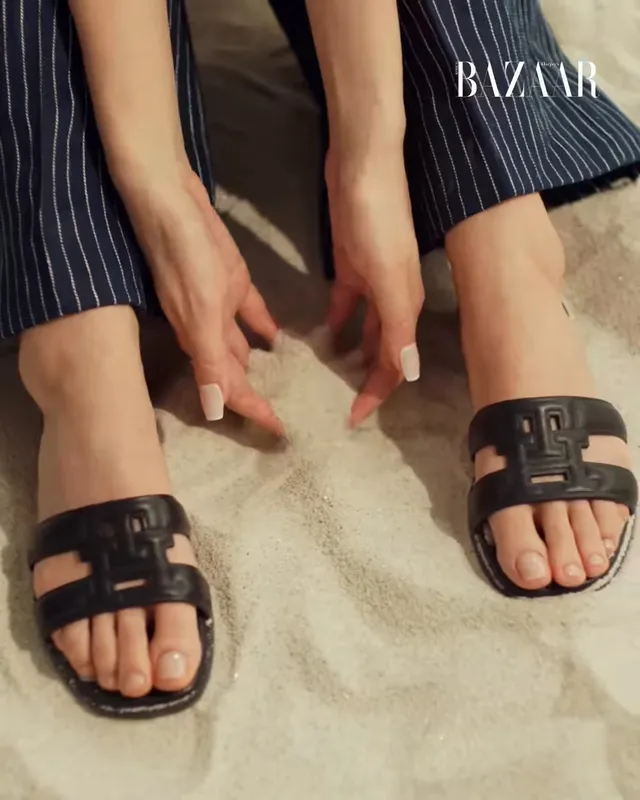 Jisoo showing black flat slides with a dark outfit during a fashion shoot.