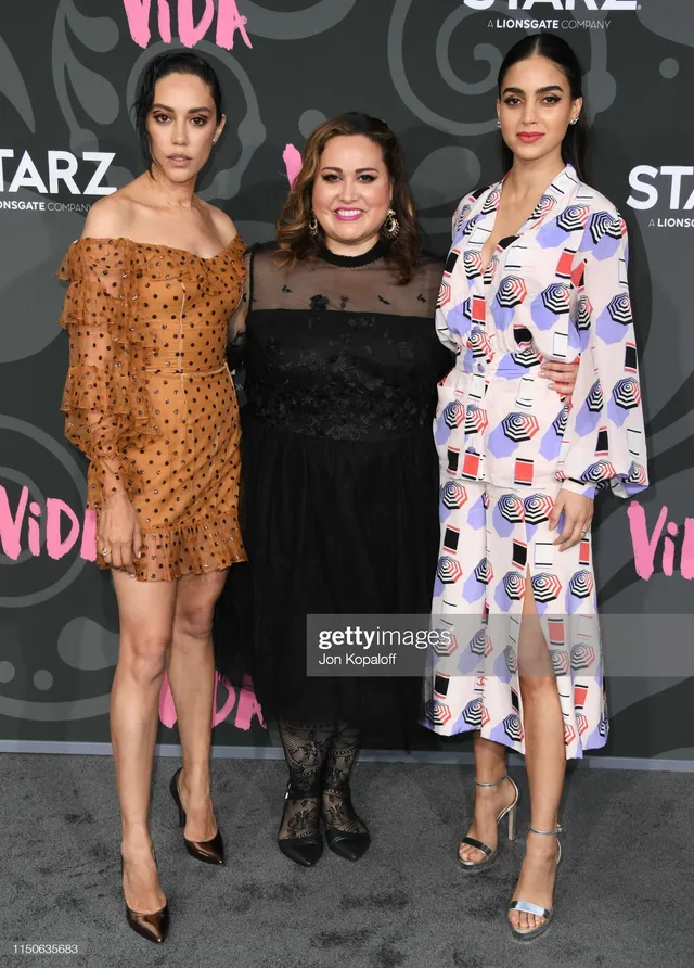 Melissa Barrera standing beside two women in a patterned outfit and heels.