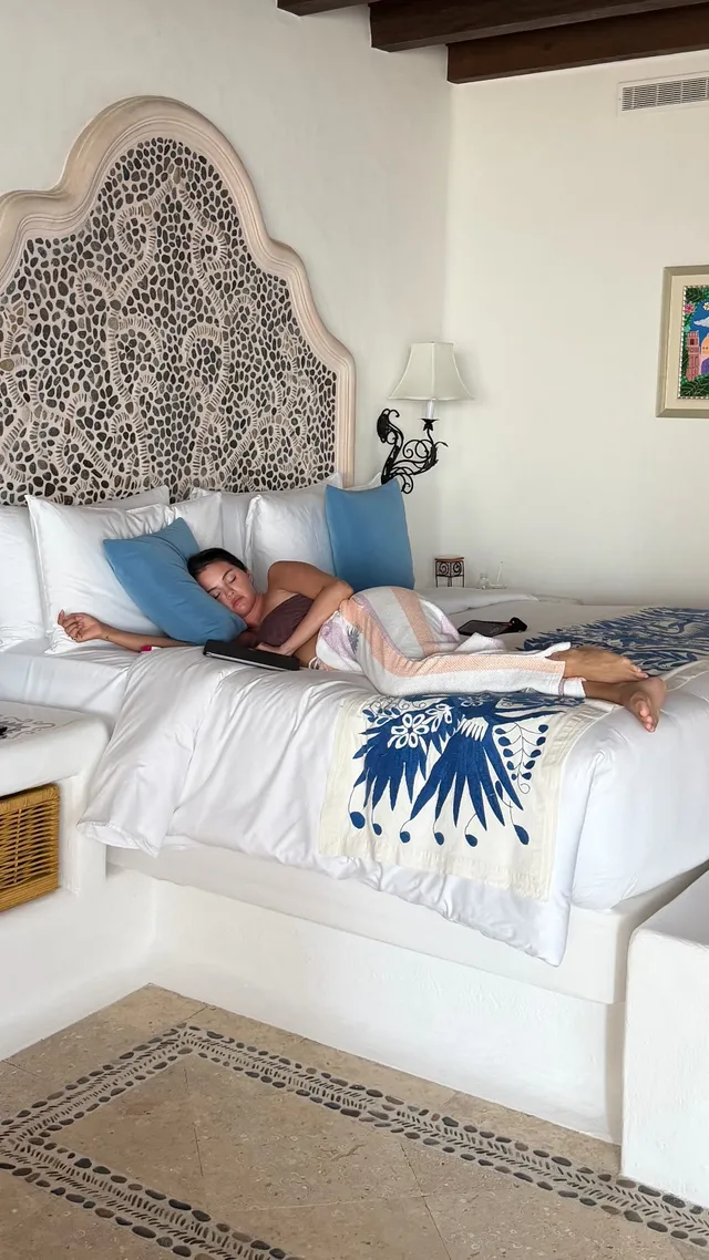 Selena Gomez: reclining barefoot on a bed in a bright bedroom.