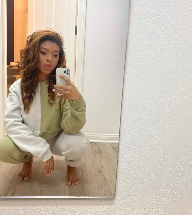 Sierra Capri taking a mirror selfie while crouching barefoot in a tracksuit.