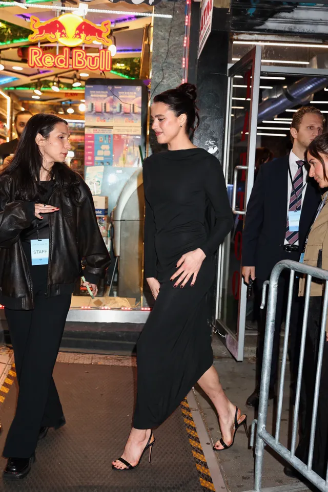 Margaret Qualley wearing a black dress and heeled sandals outside at night.