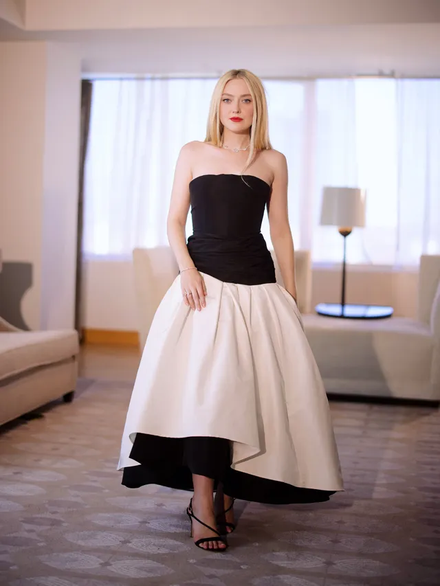 Dakota Fanning posing indoors in a black and white dress and black heels.