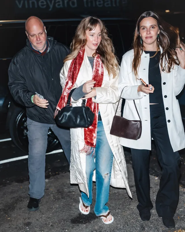 Jennifer Lawrence walking with a group in a coat and flat sandals.
