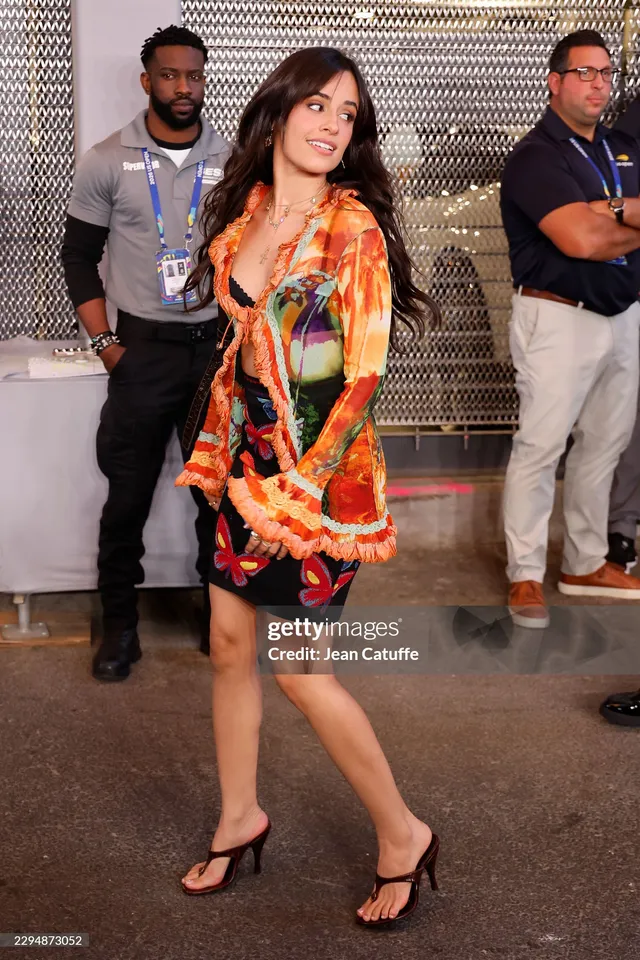 Camila Cabello walking in a colorful outfit and black heels at an event.