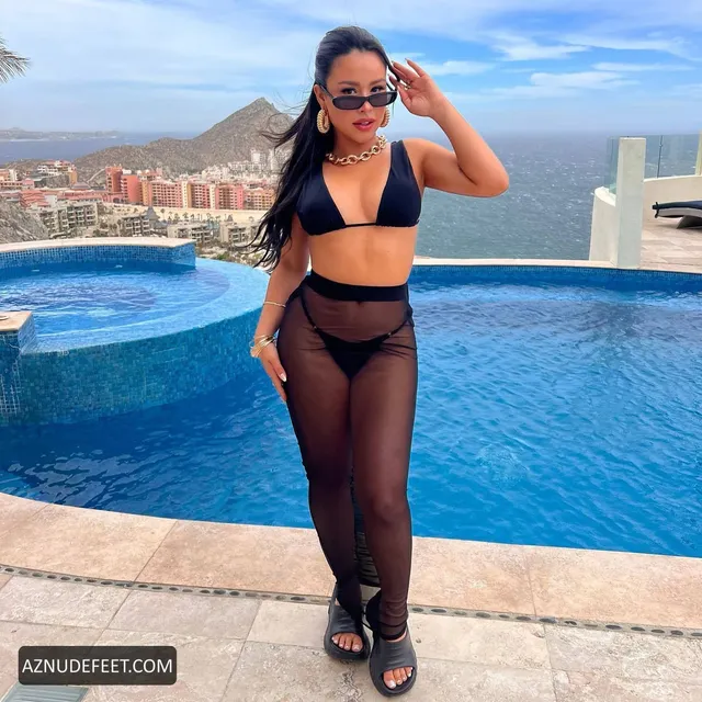 Cierra Ramirez in a black bikini top, sheer trousers and dark flats beside a rooftop pool.
