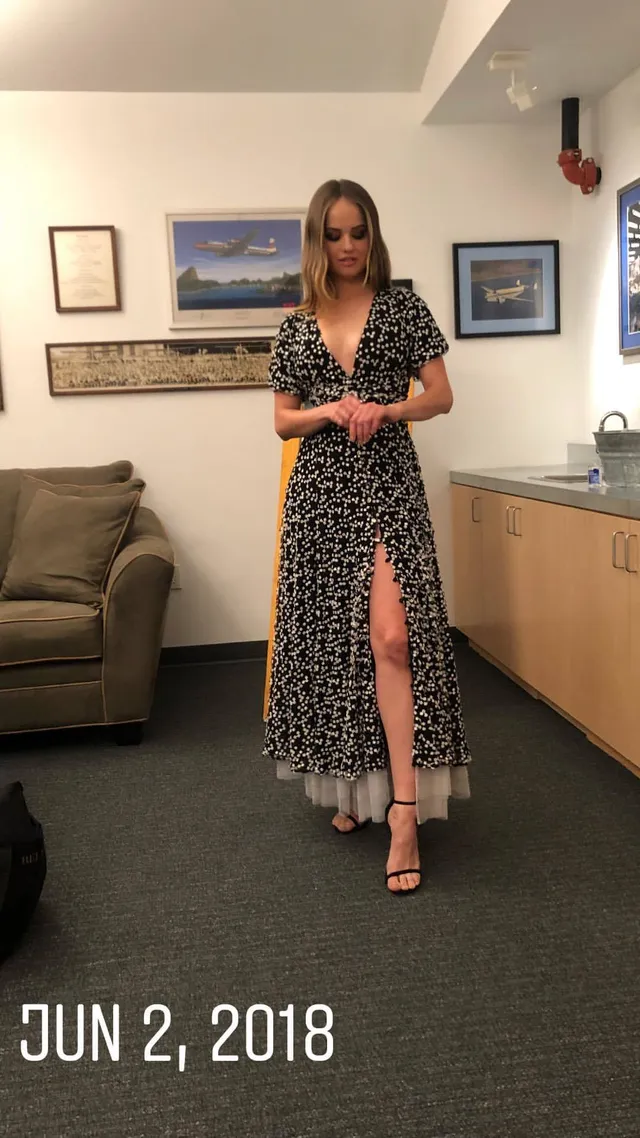 Debby Ryan wearing a patterned dress and sandals indoors.