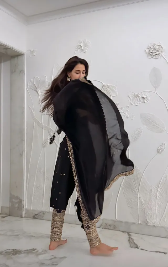 Disha Patani standing barefoot in embroidered trousers and a flowing black outfit.