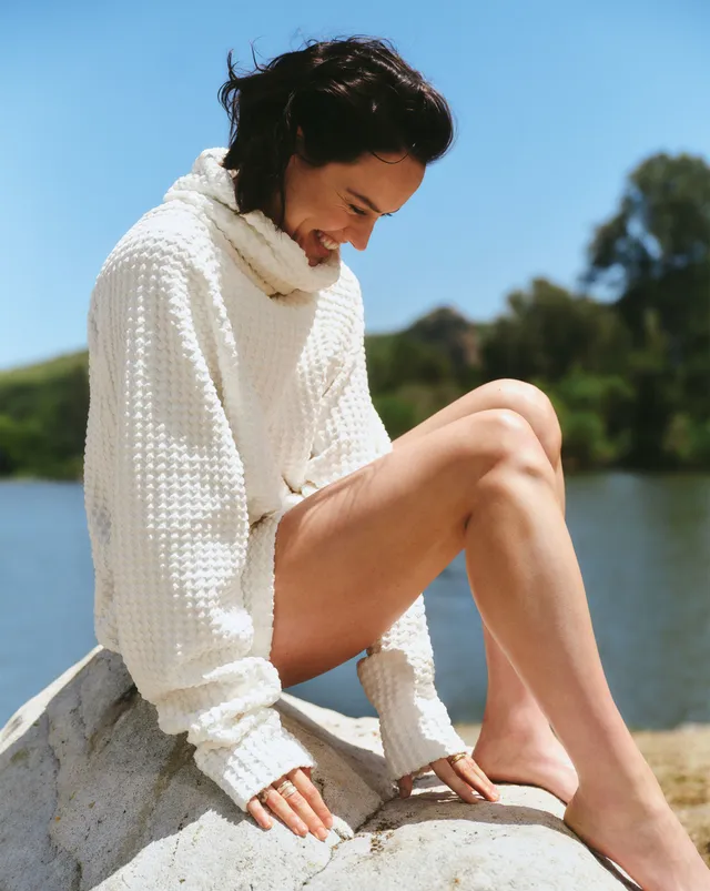 Daisy Ridley sitting outdoors in a white textured jumper.