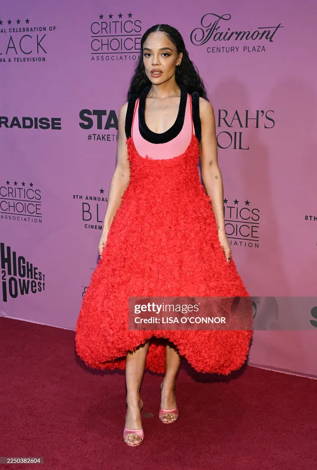 Tessa Thompson posing against a pink event backdrop.