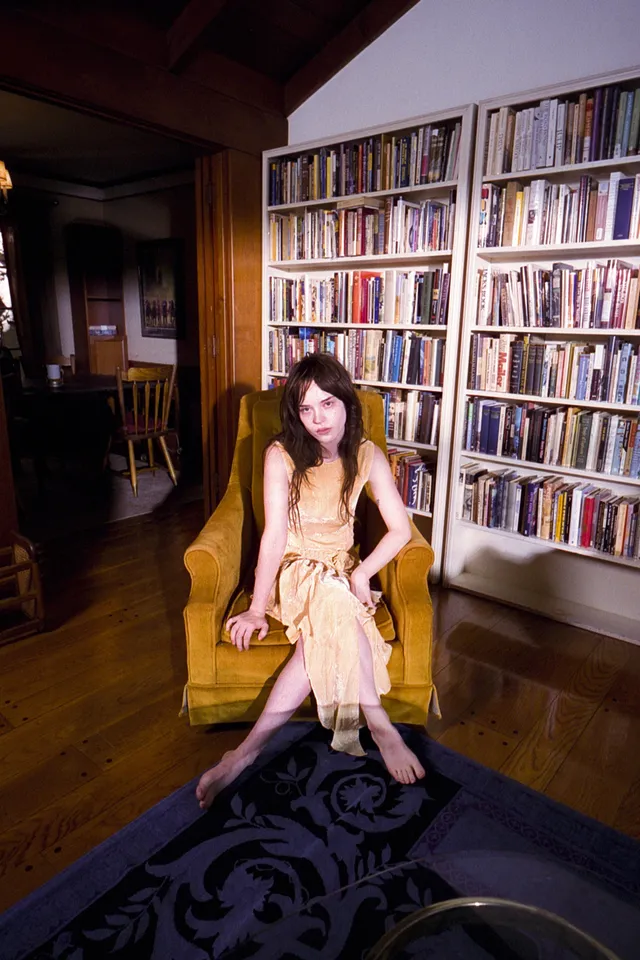 Sophie Thatcher sitting barefoot in an armchair beside shelves of records.