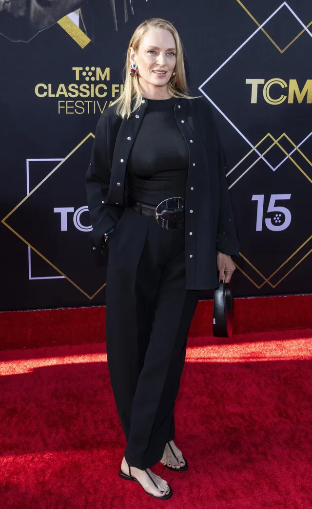 Uma Thurman wearing a black outfit and heels on a red carpet.