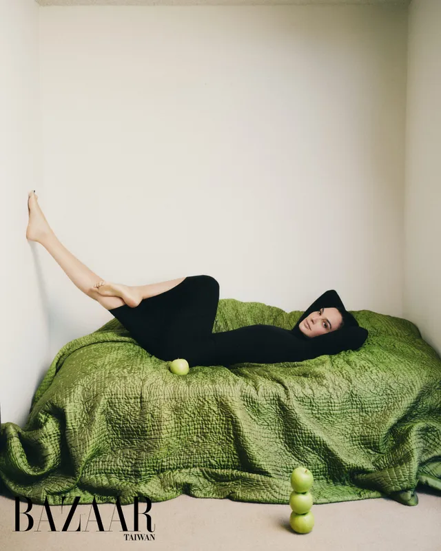 Gal Gadot reclining barefoot on a green sofa.