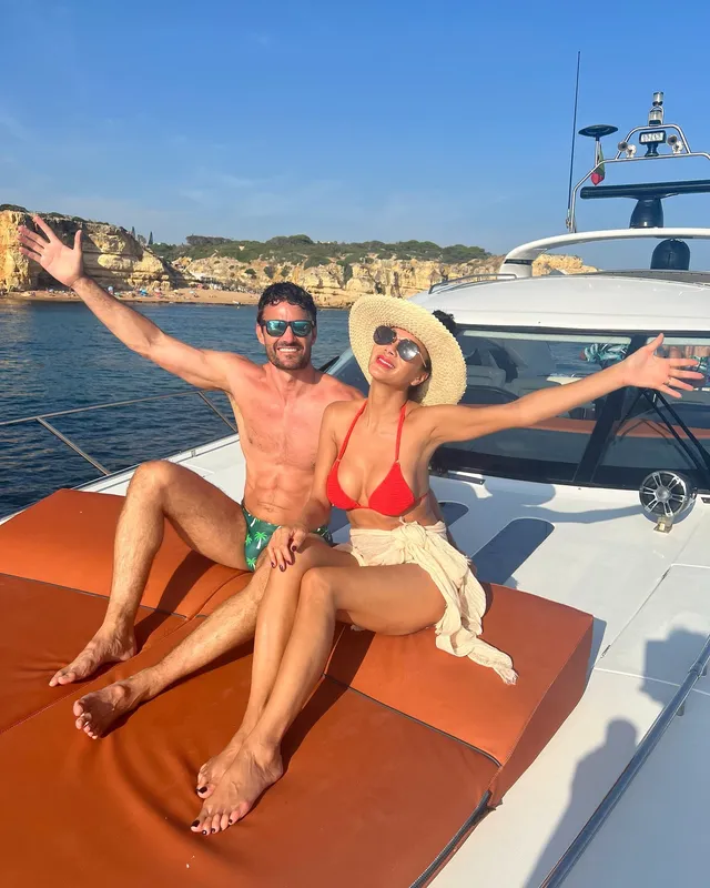 Nicole Scherzinger sitting barefoot on a boat beside another person.