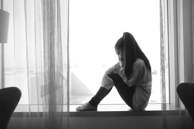 Ariana Grande seated barefoot beside a window for a monochrome portrait.