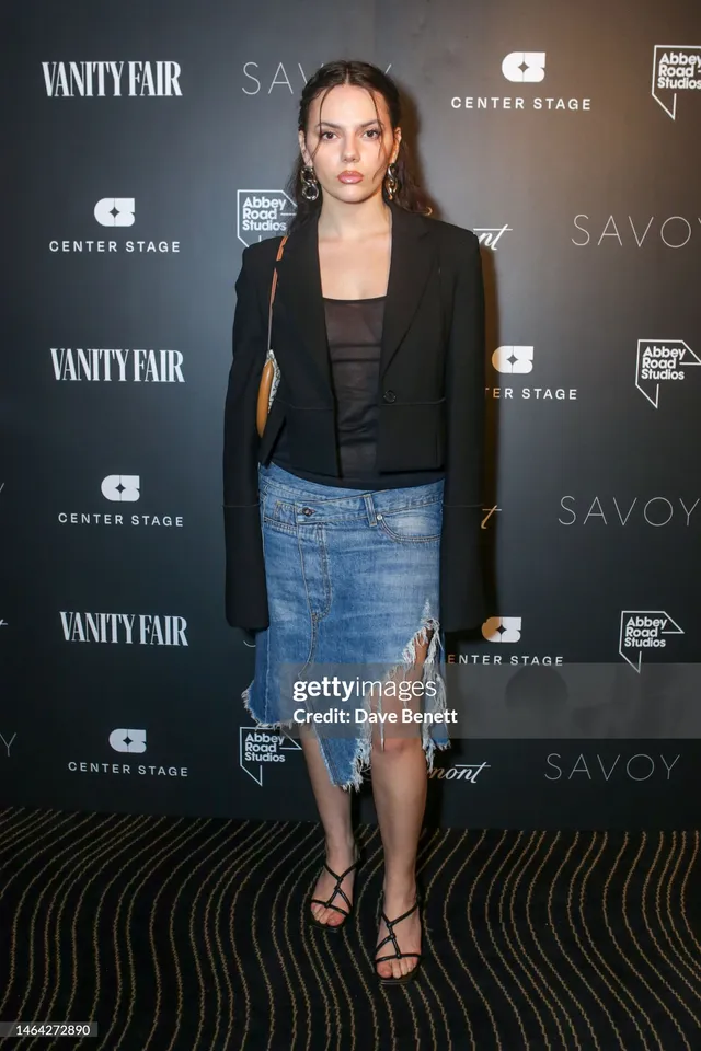 Dafne Keen standing at an event in a jacket and denim skirt with heels.