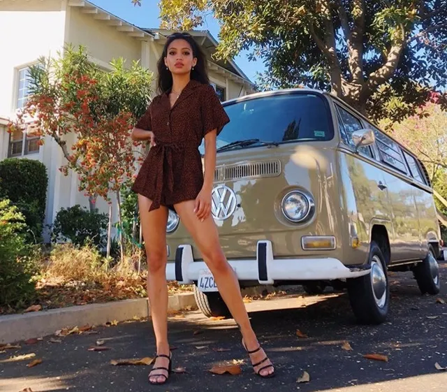 Samantha Logan standing beside a van in a short patterned outfit and black heels.
