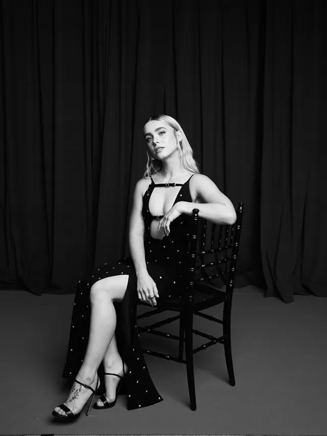 Clara Galle sitting in a chair in a black dress and heels for a monochrome portrait.