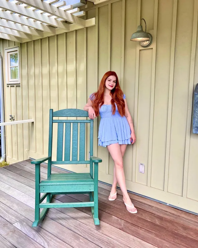 Ariel Winter standing beside a porch chair in a blue outfit.