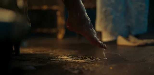 Freya Allan raising a bare heel from a wet floor in a film scene.