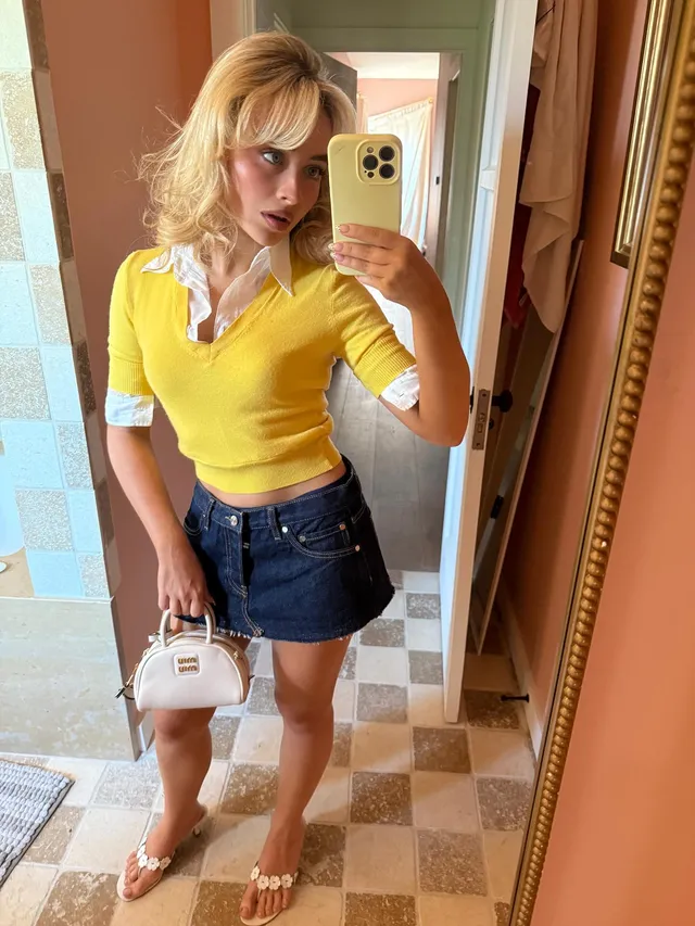 Sabrina Carpenter taking a mirror photo in a yellow top and denim skirt with heels.