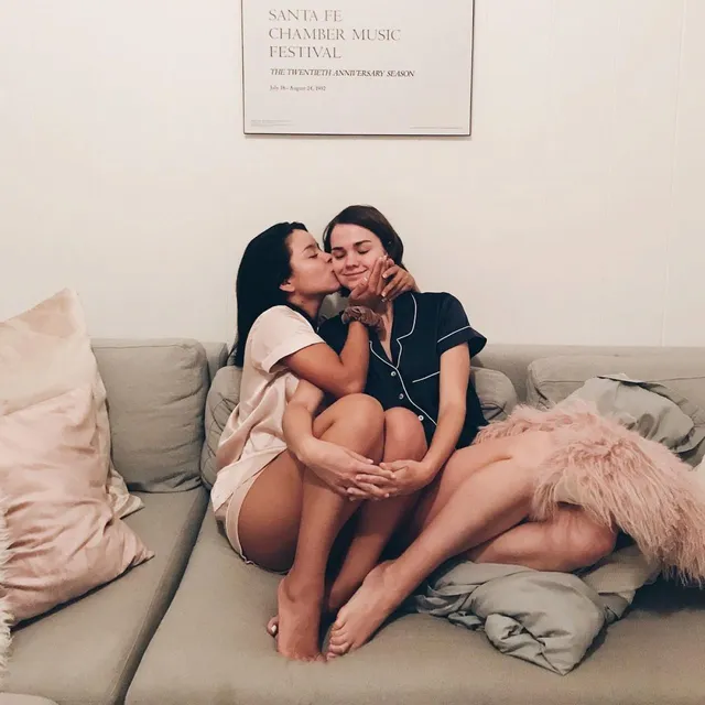 Maia Mitchell sitting barefoot with a friend on a sofa.