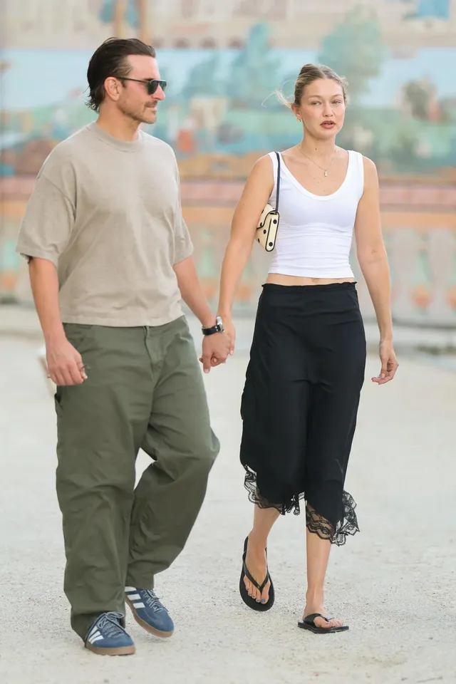 Gigi Hadid walking outside in a dark skirt and flat sandals.