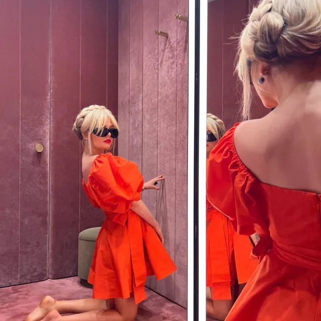 Emily Alyn Lind kneeling barefoot in an orange dress for an outdoor portrait.