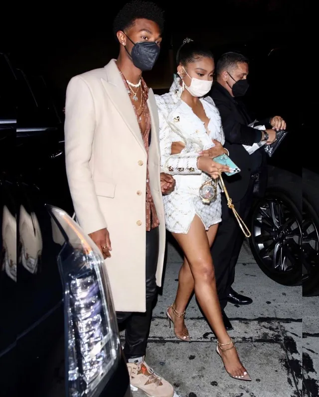 Sierra Capri walking outside beside a man in a white outfit and clear heels.
