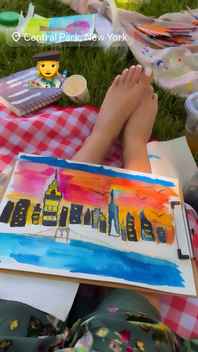 Madison Pettis shown with bare feet extended on a picnic blanket beside a painting.