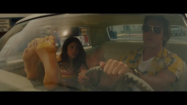 Margaret Qualley a car screen scene with feet raised beside a driver.
