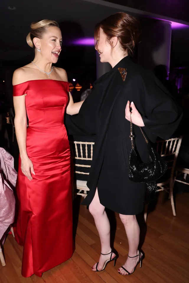 Emma Stone talking with another guest in a black dress and ankle-strap heels.