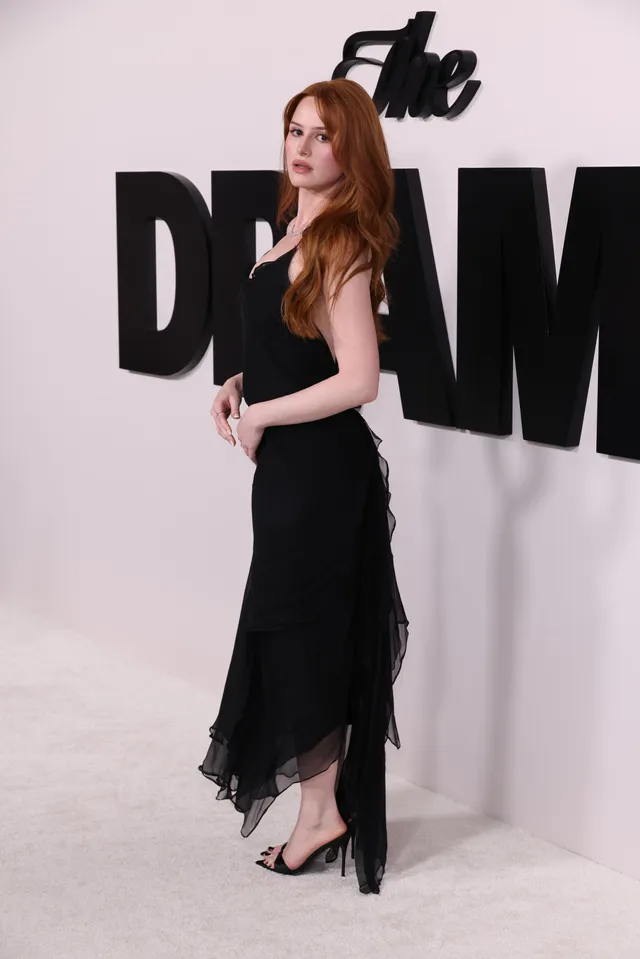 Madelaine Petsch posing in a long black dress and heels viewed from the side.