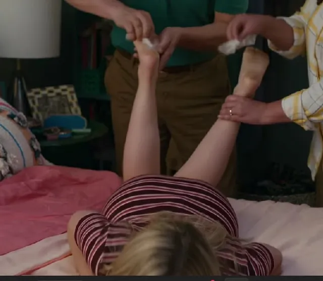 Meg Donnelly lying on a bed while two cast members hold her raised feet in a behind-the-scenes scene.