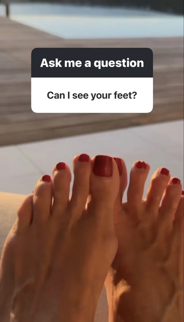 Heidi Klum showing her red-painted toenails above a wooden floor.