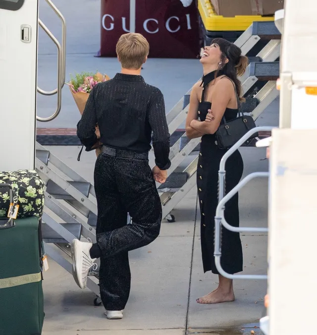 Xochitl Gomez standing barefoot beside an aircraft while holding shoes.