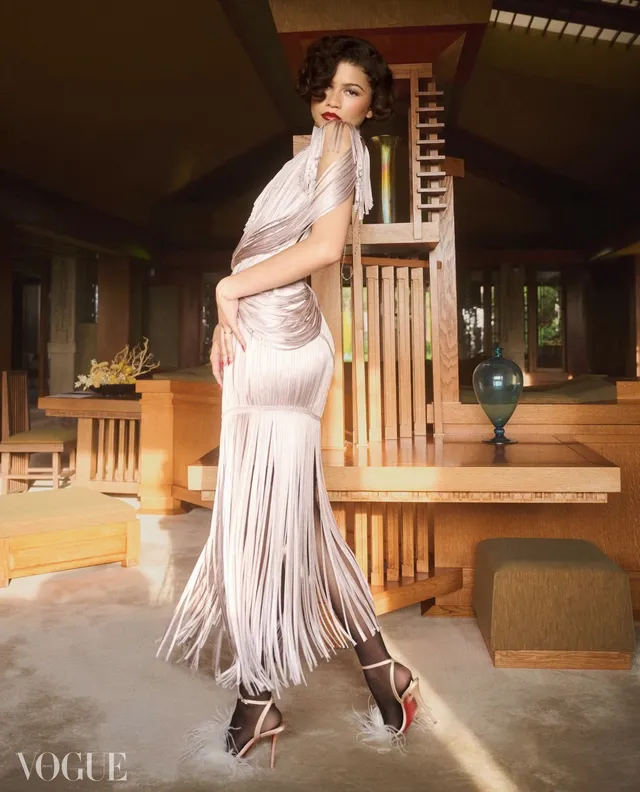 Zendaya posing beside a piano in a pale dress.